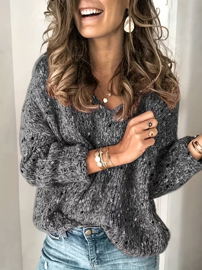 Frau in grauem Strickpullover, lächelnd, mit Schmuck und blauen Jeans, modisch, lässig.