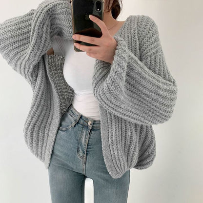 Frau in grauem Strickpullover, weiße Bluse, blaue Jeans, Smartphone, modisch, gemütlich.
