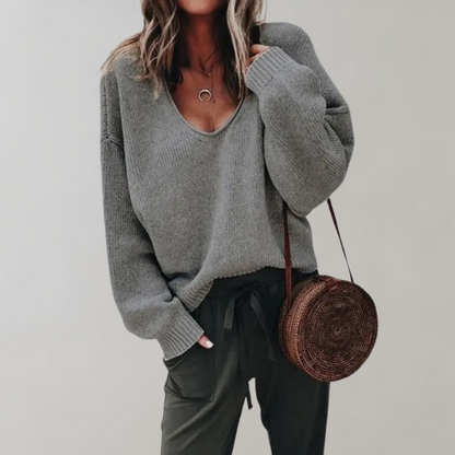 Frau in grauem Strickpullover mit rundem Strohtasche, lässiger Herbstlook.
