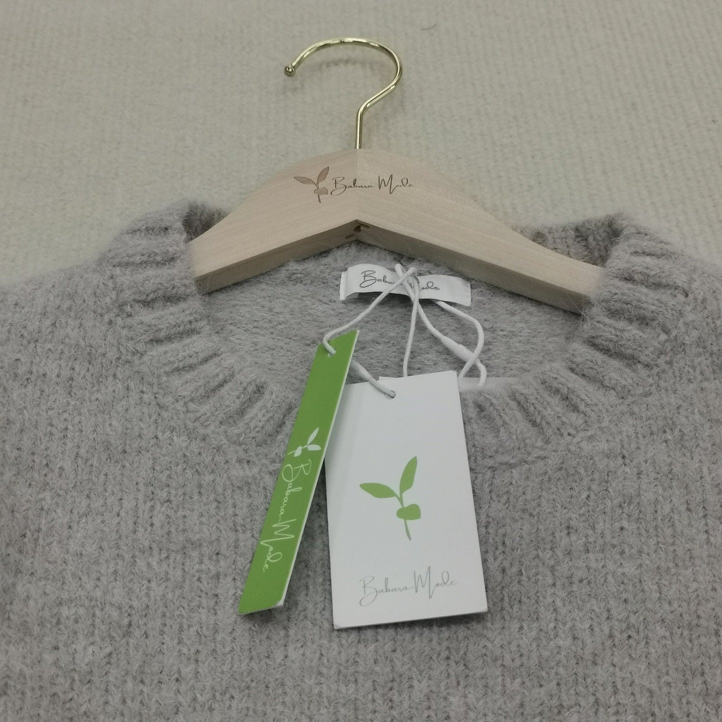 Grauer Strickpullover aus Wolle auf Holzkleiderbügel mit Etiketten, nachhaltige Mode.