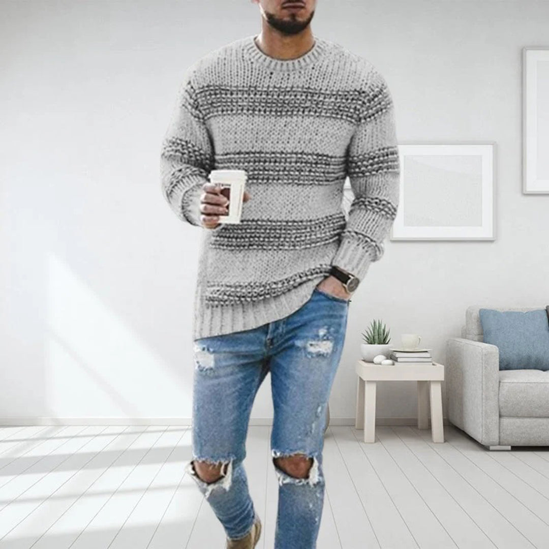 Mann in grauem Strickpullover mit Kaffeetasse, zerrissene Jeans, modernes Wohnzimmer.