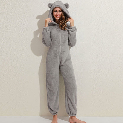 Frau in grauem Plüsch-Onesie mit Kapuze und Bärenohren, gemütliche Hausbekleidung.