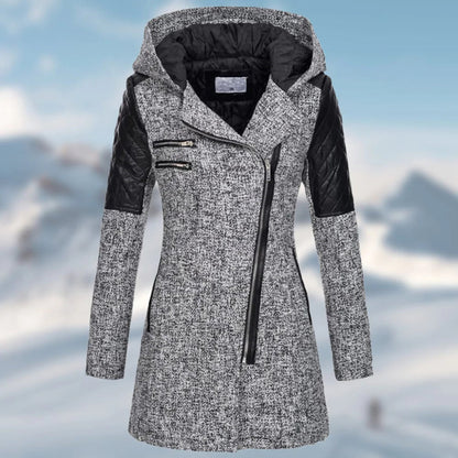 Grauer Damen-Wintermantel mit Kapuze, Reißverschlüssen und schwarzen Lederakzenten vor Schneehintergrund.