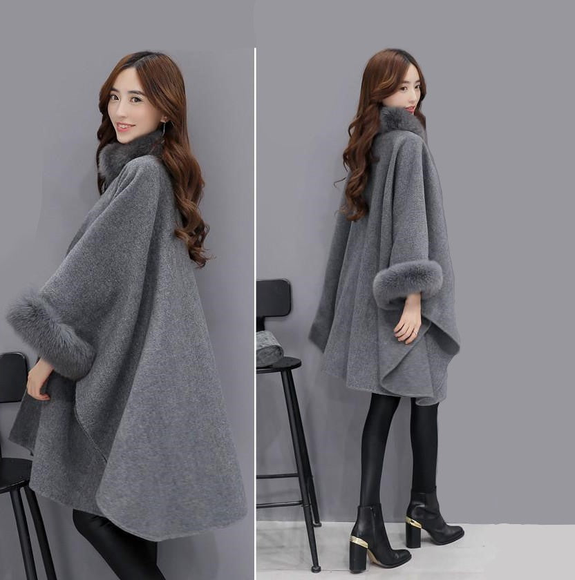 Frau in grauem Wollponcho mit Kunstpelzkragen und -ärmeln, modisch, elegant, Winterkleidung.
