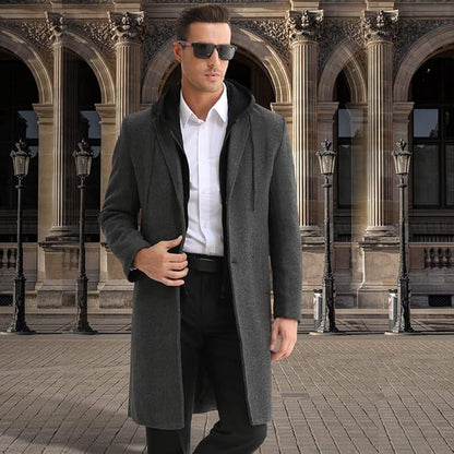 Mann in grauem Wollmantel, weißem Hemd, Sonnenbrille, vor historischer Architektur.