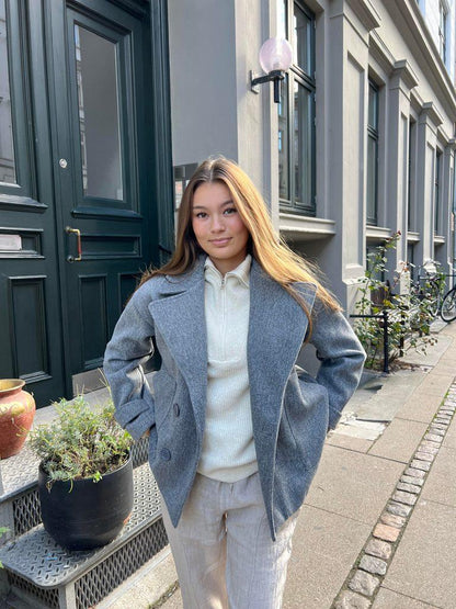 Frau in grauem Wollmantel und beiger Hose vor Stadthaus, Mode Herbst Winter 2023.