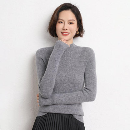Frau in grauem Kaschmirpullover, Rollkragen, lächelnd, vor weißer Wand.