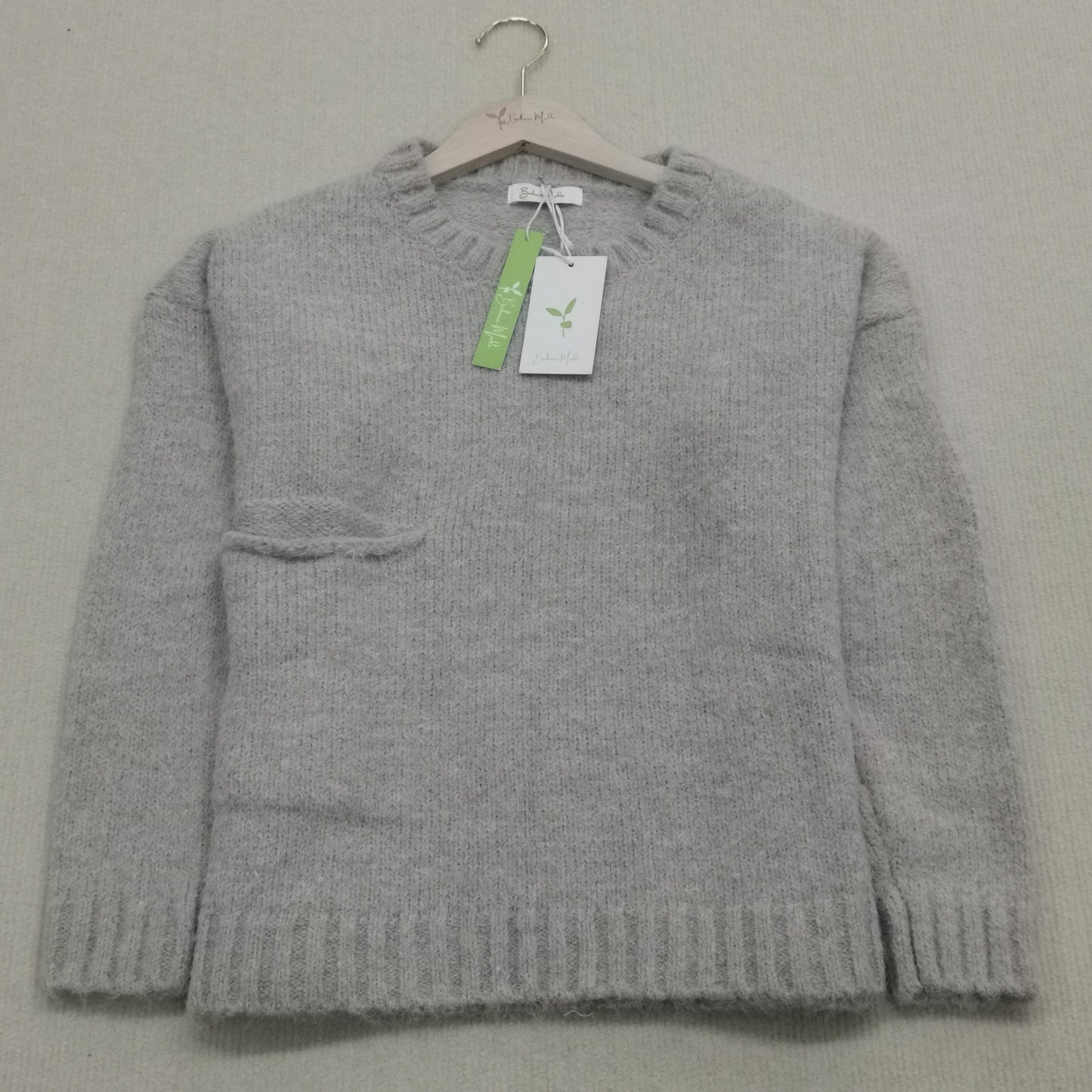 Grauer Wollpullover auf Bügel, Rundhalsausschnitt, Etikett, weiches Material, Damenmode.