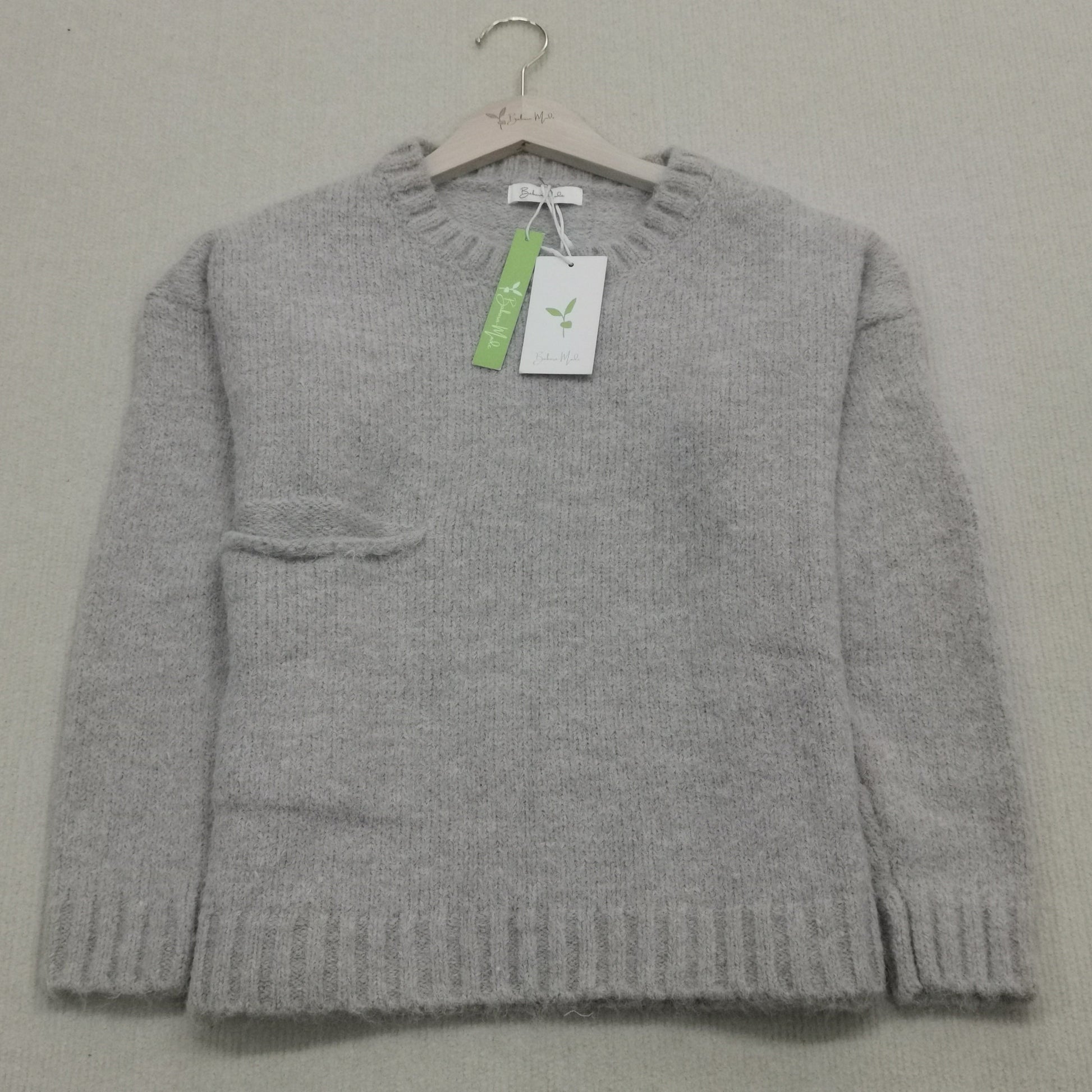 Grauer Wollpullover auf Bügel, Rundhalsausschnitt, Etikett, weiches Material, Damenmode.
