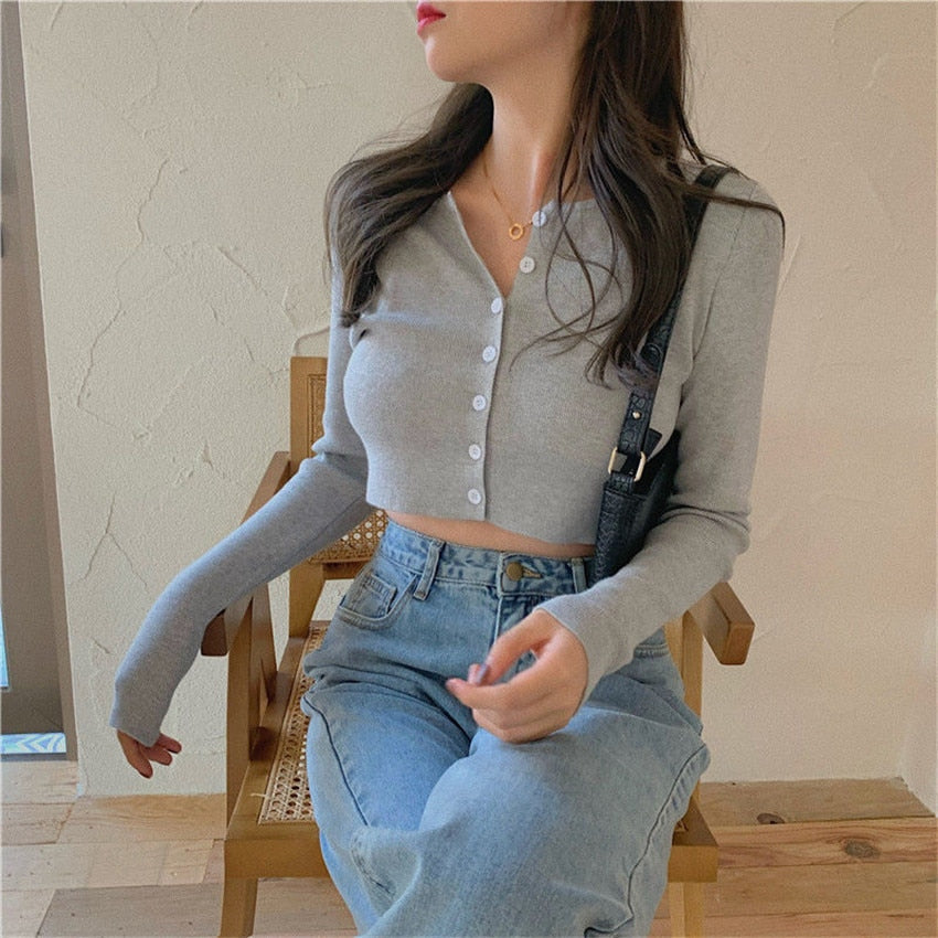 Frau in grauem Crop-Cardigan und blauer Jeans sitzt auf Holzstuhl, modisch, lässig.