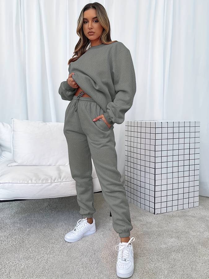 Frau in grauem Jogginganzug, weiße Sneaker, modernes Wohnzimmer, gemütliche Mode.