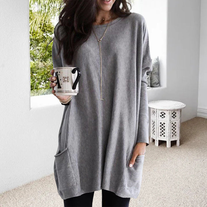 Frau in grauem Oversize-Pullover mit Tasse, gemütliche Mode, Wohnzimmer, lässiger Stil.