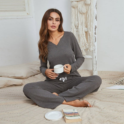Frau in grauem Pyjama mit Tasse, sitzt auf Bett, gemütliche Nachtwäsche, Innenraum.