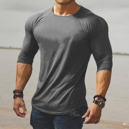 Mann in grauem, enganliegendem Langarmshirt am Strand, muskulös, modisch, Freizeitkleidung.