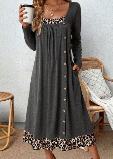 Frau in grauem Kleid mit Leopardenmuster, hält Kaffeetasse, sitzt auf Rattanstuhl.