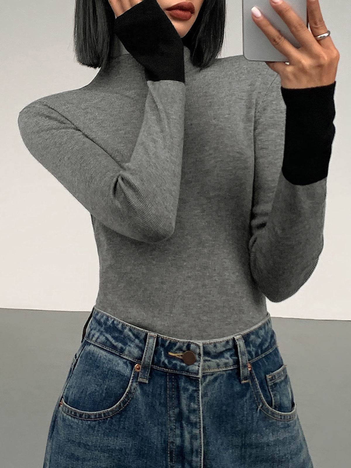 Frau in grauem Rollkragenpullover und blauer Jeans, Selfie, modisch, minimalistisch.