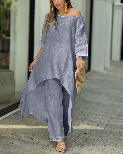 Frau in grauem Leinenkleid mit asymmetrischem Schnitt, gelbe Ohrringe, Strohtasche.