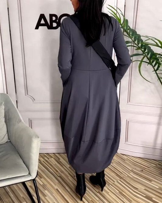 Frau in grauem Maxikleid mit schwarzer Tasche, moderne Mode, elegantes Design, Innenraum.