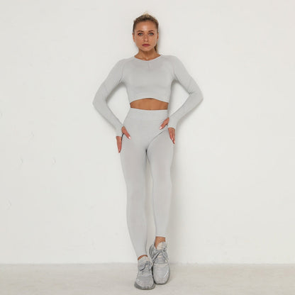 Frau in grauem nahtlosem Sport-Set, Langarm-Top und Leggings, Fitnessmode, Studioaufnahme.