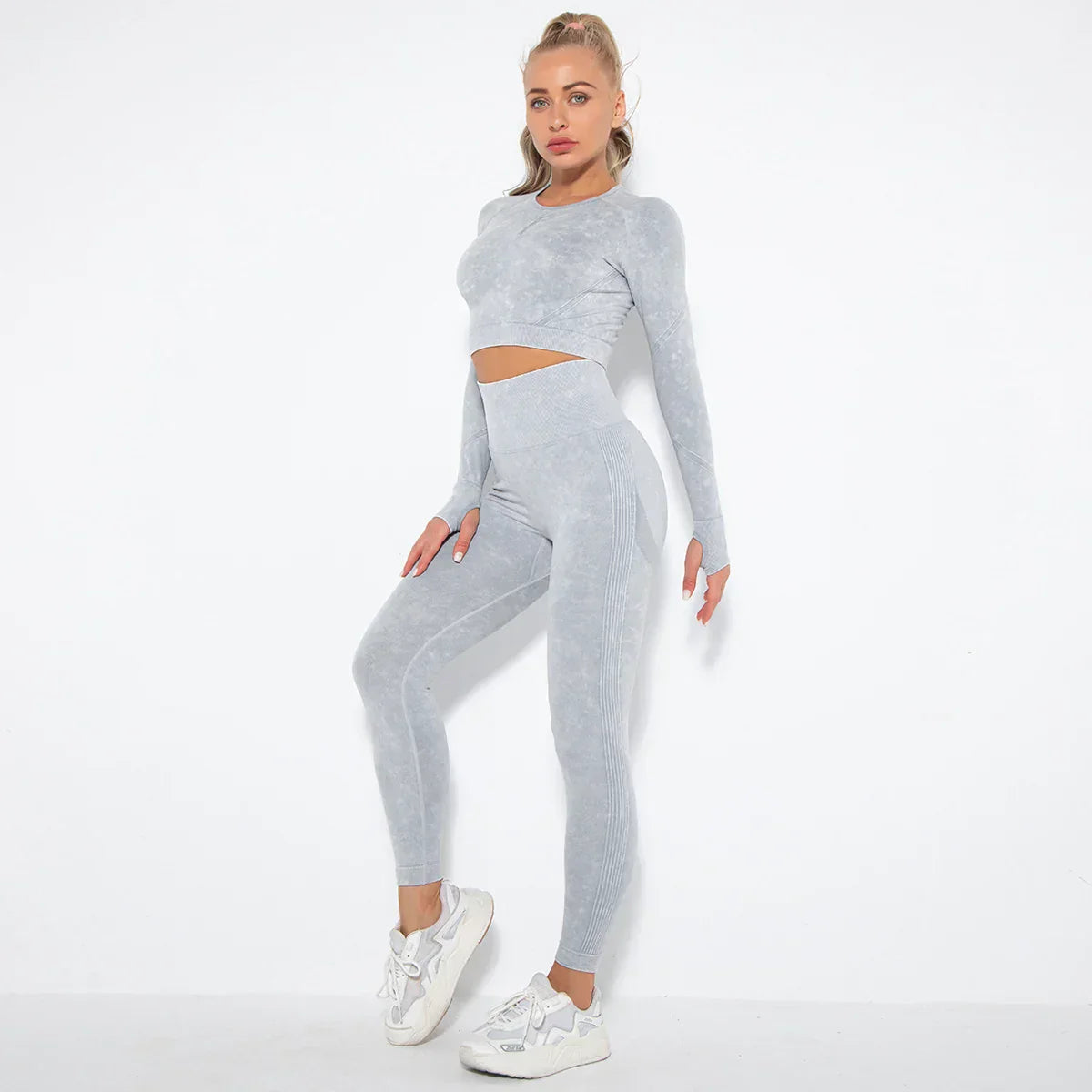 Frau in grauem nahtlosem Sport-Set, langärmeliges Oberteil, Leggings, weiße Turnschuhe.