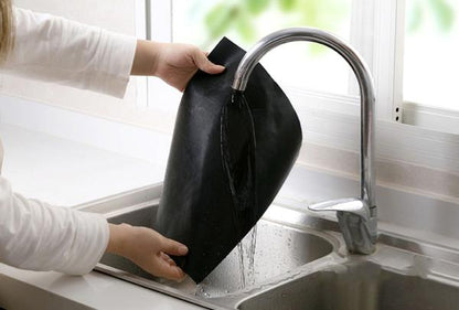 Person wäscht schwarze Grillmatte unter Wasserhahn in moderner Küche.
