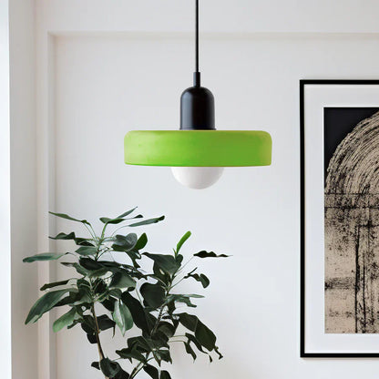 Moderne grüne Pendelleuchte mit schwarzem Sockel, hängend über Zimmerpflanze, minimalistisch.