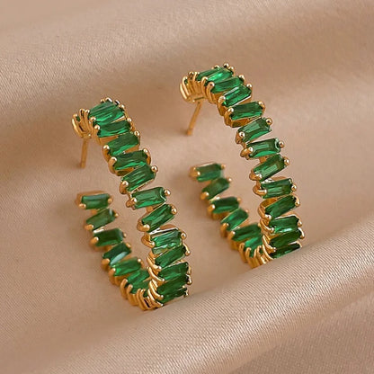 Goldene Creolen mit grünen Edelsteinen auf beigem Stoff, eleganter Schmuck, modische Ohrringe.