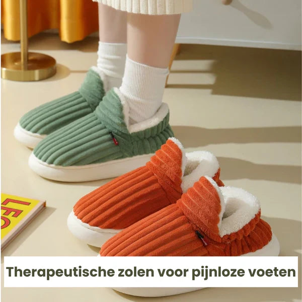 Grüne und orange Plüschhausschuhe mit therapeutischen Sohlen auf Teppichboden.