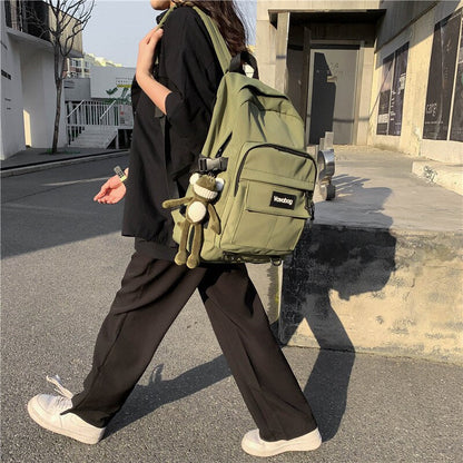 Frau mit grünem Rucksack und Plüschanhänger, lässige Kleidung, urbaner Hintergrund.