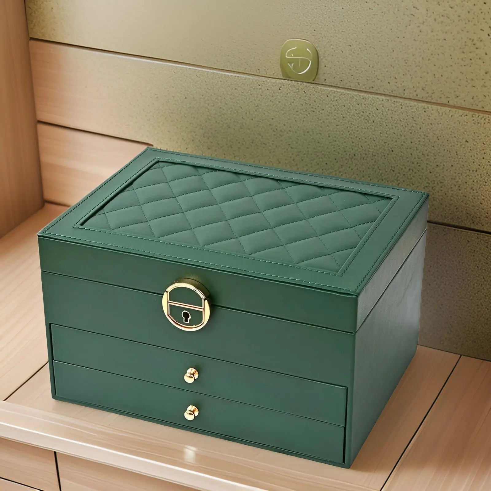 Grüne Schmuckschatulle aus Leder mit Rautenmuster und goldenen Griffen auf Holzregal.