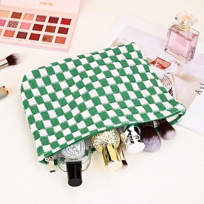 Grün-weiß karierte Kosmetiktasche mit Make-up-Pinseln und Parfümflaschen auf hellem Hintergrund.
