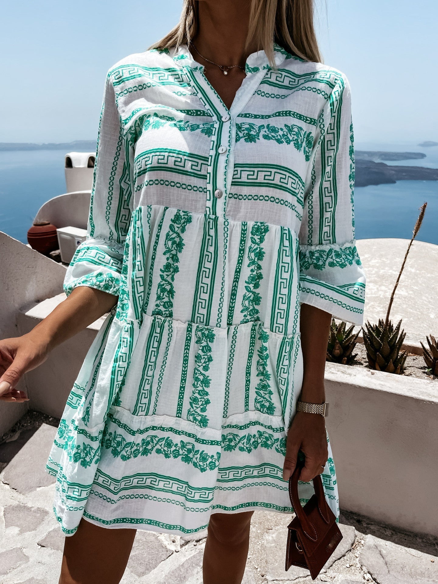 Frau in weißem und grünem Sommerkleid mit griechischem Muster, Meerblick im Hintergrund.