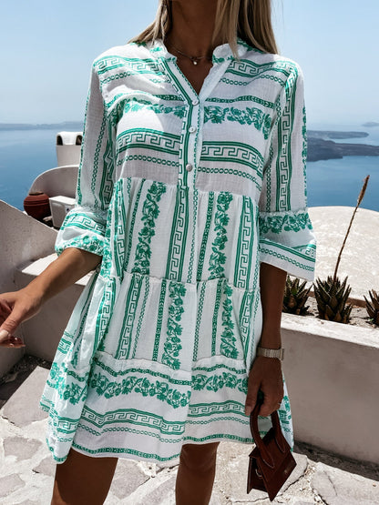 Frau in weißem und grünem Sommerkleid mit griechischem Muster, Meerblick im Hintergrund.