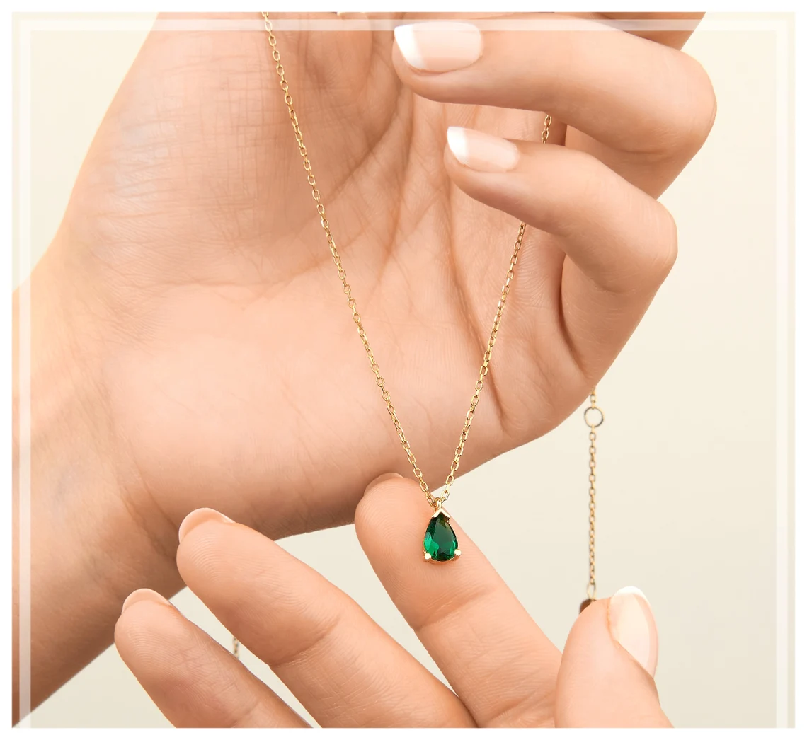 Frau hält goldene Halskette mit grünem Edelstein-Anhänger, eleganter Schmuck, Nahaufnahme.