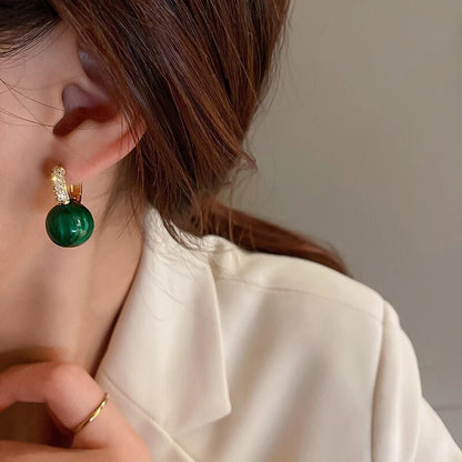 Ohrring mit grünem Edelstein und goldenen Details, getragen von Frau, eleganter Schmuck.