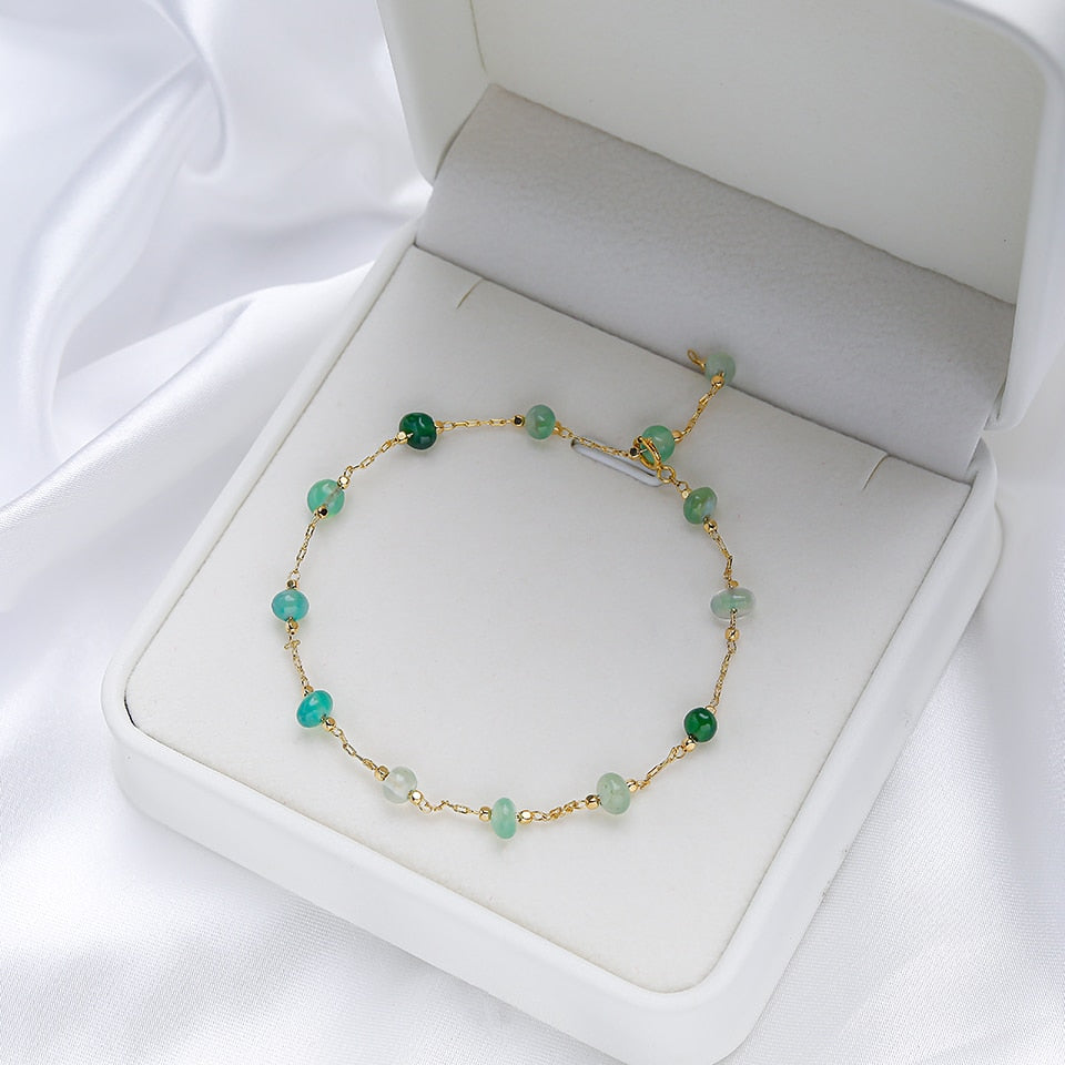 Goldenes Armband mit grünen Edelsteinen in weißer Schmuckschatulle, elegantes Design.