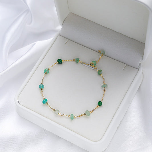 Goldenes Armband mit grünen Edelsteinen in weißer Schmuckschatulle, elegantes Design.