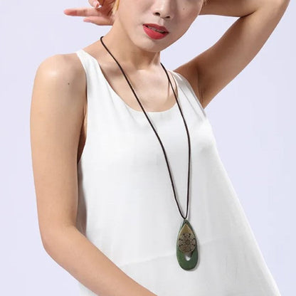 Frau mit weißem Kleid und grünem Anhänger-Halskette, modisches Accessoire, eleganter Schmuck.