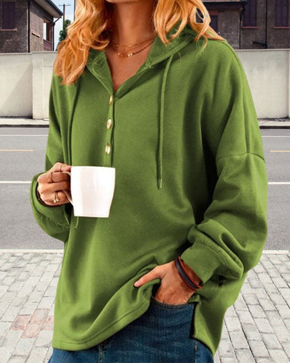 Frau in grünem Hoodie mit Kapuze hält weiße Tasse, lässige Mode, Straßenhintergrund.