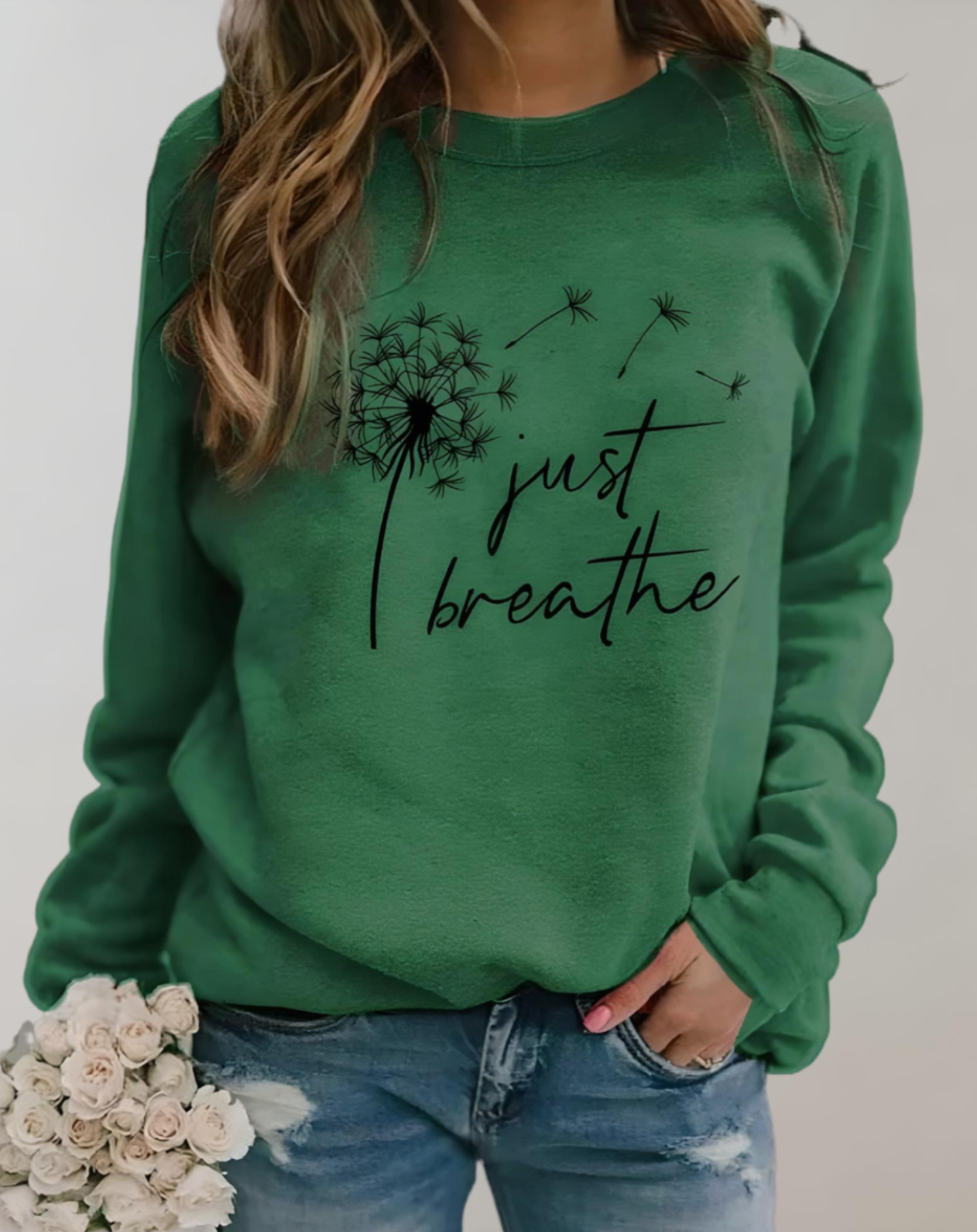 Frau in grünem "Just Breathe" Pullover, Löwenzahn-Motiv, lässige Mode, Jeans, Blumenstrauß.