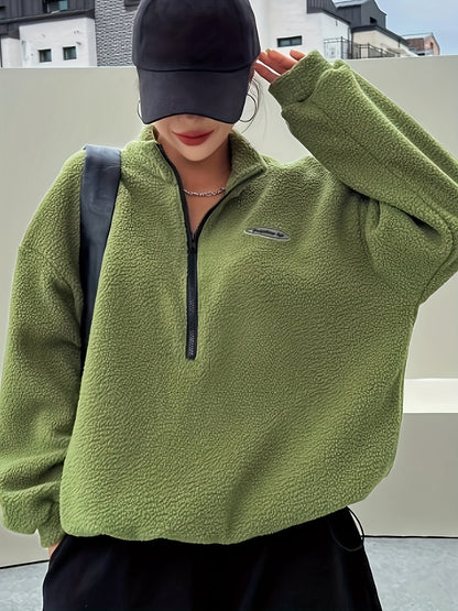 Frau in olivgrünem Fleece-Pullover mit Reißverschluss und schwarzer Kappe, urbaner Hintergrund.