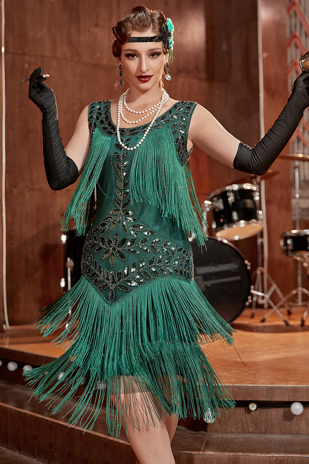 Frau im grünen Charleston-Kleid mit Fransen, Perlenkette, schwarzen Handschuhen, Retro-Stil.