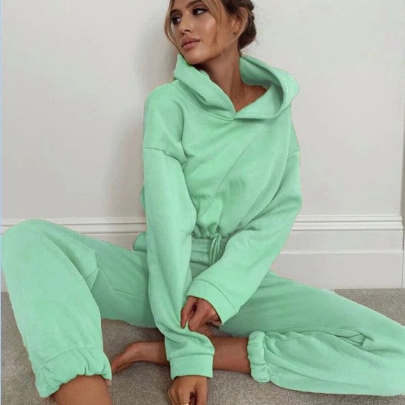 Frau in mintgrünem Jogginganzug, Kapuzenpullover und Jogginghose, gemütliche Freizeitmode.