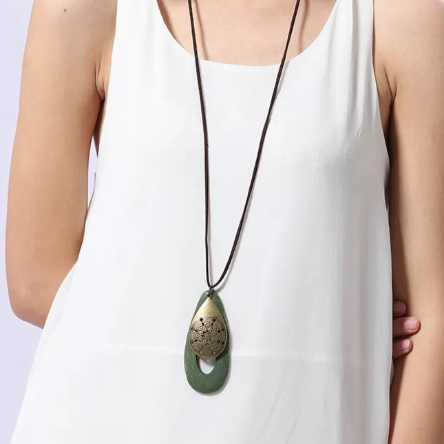 Damenkette mit grünem Anhänger, Holz und Metall, lang, modisch, Boho-Stil, auf weißem Kleid.