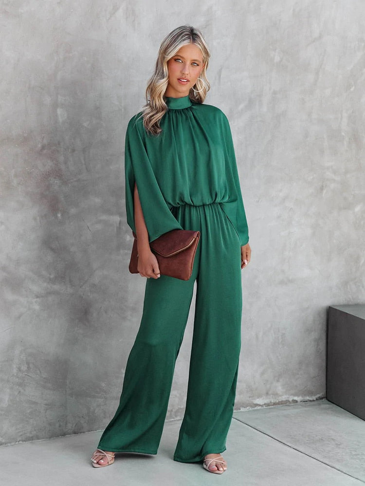 Frau im grünen Jumpsuit mit brauner Clutch vor grauer Wand, elegante Mode, Abendgarderobe.