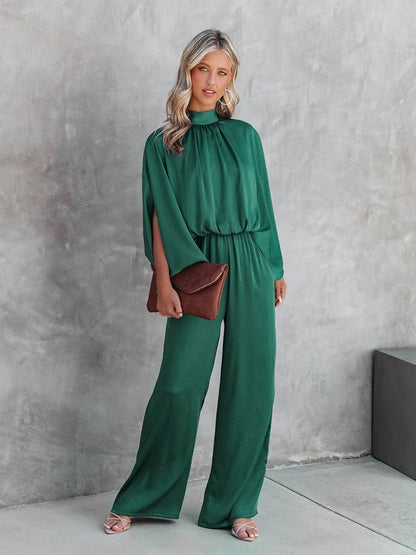 Frau im grünen Jumpsuit mit brauner Clutch vor grauer Wand, elegante Mode, Abendgarderobe.