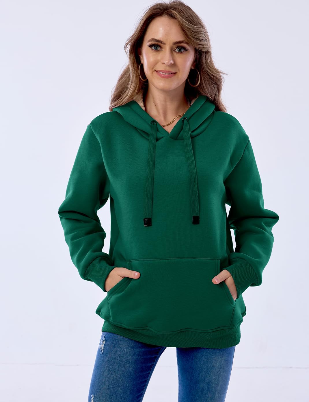 Frau in grünem Kapuzenpullover, Kängurutasche, Jeans, lächelnd, Freizeitmode, Damenbekleidung.