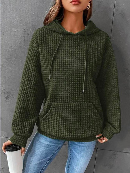 Frau in grünem Kapuzenpullover, gesteppter Stoff, lässiger Stil, hält Kaffeebecher.
