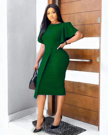 Frau in elegantem, grünem Kleid vor Holztür, schwarze Tasche, High Heels, Modefotografie.