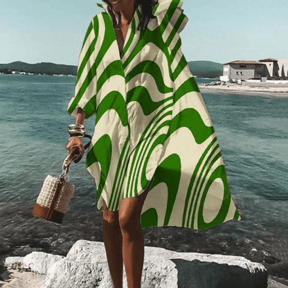 Frau in grün-weißem, gemustertem knielangem Kleid am Meer, Sommermode, stilvoll.